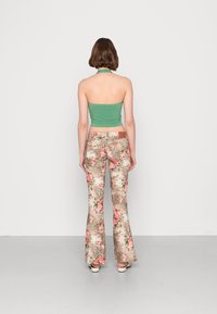 Top cropped halter verde emparelhado com calças flare apresentando um padrão de estampas florais e animais em castanho, rosa e bege.