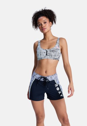 Dwuczęściowy strój kąpielowy z wzorzystym stanikiem typu bralette o okrągłym dekolcie i czarnymi szortami na sznurku z białym napisem "ROXY" po boku.