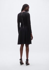 Must kleit pikkade varrukatega, kellukakujulise seelikuga ja nähtava seljapoolse tõmblukuga. Kanda mustade pahkluu-saabastega, millel on pandlad ja paelad.