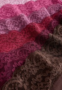 Rangs de tissu en dentelle pliée dans différentes nuances de rose, rouge, violet et marron avec des motifs floraux complexes.