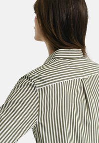 Striped shirt featuring green and white vertical stripes, with a collared neck, buttoned back pleat, and smooth, lightweight fabric.