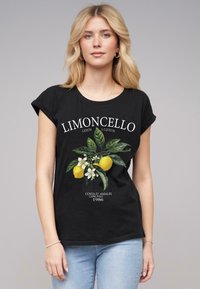 Svart t-shirt i bomull med en grafik av citroner och blommor, med texten "Limoncello" ovanför och "Costa d'Amalfi, Capri, Italien, 1986" nedanför.