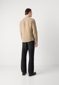 Camisa de lino color beige con cuello y puños abotonados, combinada con pantalones anchos negros. La tela tiene un acabado texturizado y un corte holgado.