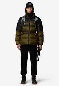 Puchowa, oliwkowo-zielona i czarna kurtka ocieplana z wysokim kołnierzem, plecak, czarne spodnie i brązowe buty turystyczne. Akcesoria obejmują kijki trekkingowe.