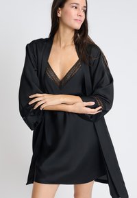 Robe in satin nero in stile kimono con dettagli in pizzo sul colletto e sulle maniche, dalla vestibilità comoda e dalla texture liscia.