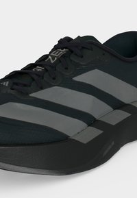 Μαύρο αθλητικό παπούτσι Adidas με τρεις γκρι ρίγες και μαύρα κορδόνια, με το κείμενο "LIGHTSTRIKE PRO" στη σόλα.
