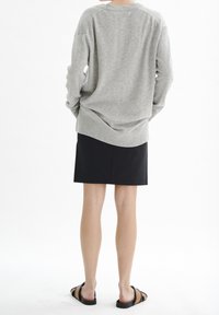 Pull en tricot gris à coupe décontractée, avec un col et un ourlet côtelés, associé à une jupe noire et des sandales plates noires. Texture lisse sur l'ensemble.