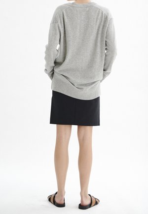 Pull en tricot gris à coupe décontractée, avec un col et un ourlet côtelés, associé à une jupe noire et des sandales plates noires. Texture lisse sur l'ensemble.