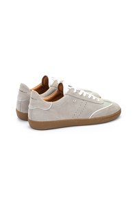 Zapatillas de ante gris claro con suela de goma, cordones blancos, detalles perforados y acentos marrones en la parte trasera y en la lengüeta.