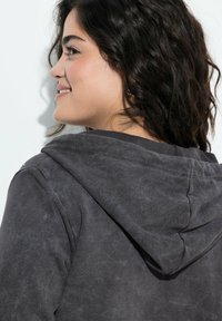 Sudadera gris oscura con un acabado texturizado, que presenta una capucha, costuras visibles y sutiles acentos en los hombros.