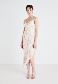 Blomstertrykt kjole med peplum-design, med volang-lag, justerbare spaghetti-stropper og asymmetrisk kant i myke pastellfarger.