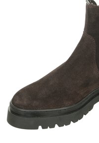 Dunkelbraune Wildleder-Stiefelette mit einer abgerundeten Zehe und einer dicken schwarzen Gummisohle, die mit einem strukturierten Profilmuster versehen ist. Schickes und modernes Design.