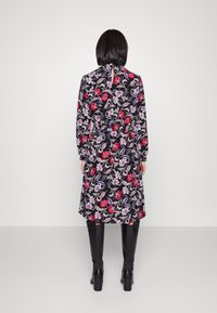 Černé květinové šaty s červenými a fialovými květy, dlouhými rukávy, nabraným pasem a detaily na zádech ve tvaru klíčové dírky, doplněné nadkolenními černými botami.