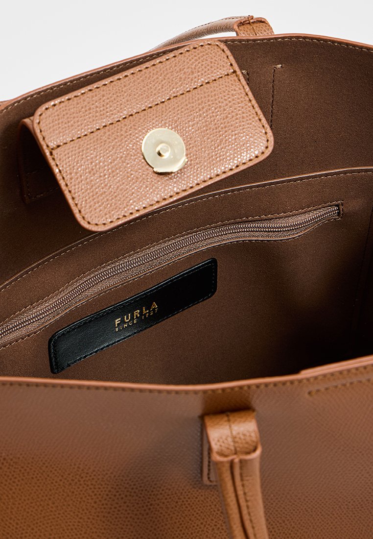Wnętrze brązowej skórzanej torebki na ramię z zasuwaną kieszonką i klapką zamykaną na złoty zatrzask, z czarną metką ze złotym napisem.
