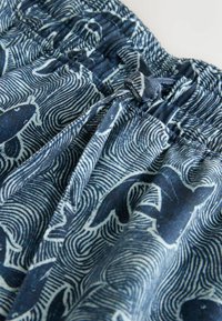 Rugalmas derékrészű anyag tengerészkék és fehér absztrakt hal- és hullámmintákkal, középen megkötött húzózsinórral.