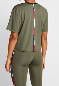 Olivgrön kortärmad topp med en kortad design, med en randig accent i rött, vitt och blått längs mittbaksidan.