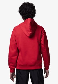 Felpa rossa con cappuccio regolabile. Tessuto morbido, polsini e orlo a costine, design semplice. Indossata con pantaloni cargo scuri.