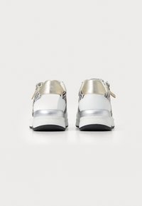 Sneaker bianchi con dettagli metallici argento e un tallone dorato, caratterizzati da un motivo a strisce zebra sui lati e una suola nera resistente.