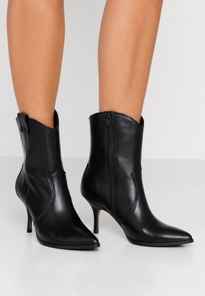 Bottines en cuir noir avec un bout pointu, une texture lisse et un talon haut élancé. Caractéristiques d'une fermeture éclair sur le côté et d'un design structuré.