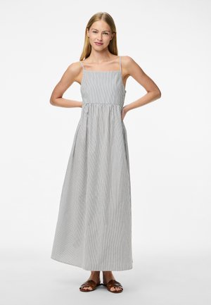 Sukienka maxi w paski, lekki materiał, taliowane w pasie, cienkie ramiączka, pionowe czarno-białe paski, długość do kostek, zestawiona z brązowymi sandałami.