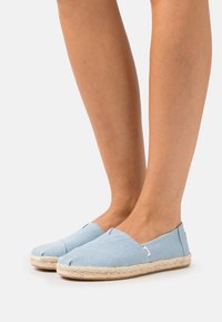 Espadrilles de lona azul claro con suela de yute trenzada. Presentan una punta redondeada y un diseño sin cierres, con mínimos acentos de costura.