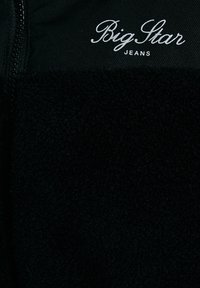 Must värviline fliispulli, millel on tõmblukk, omab pehmet tekstuuri ning sellel on valge "Big Star Jeans" logo, mis asub kaela lähedal.