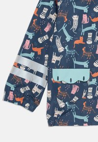 Giubbotto resistente all'acqua in tessuto blu scuro con un motivo giocoso di gatti e cani colorati. Include una tasca azzurra e strisce riflettenti.