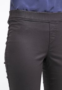 Svarta slim-fit byxor i en mjuk tygblandning, med en platt midja och ton-i-ton sömmar. Inga synliga fickor eller påfallande detaljer.