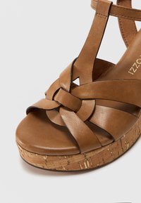 Sandali platform in pelle marrone con design a fascia intrecciata, dotati di una suola con texture in sughero e finitura in pelle liscia. Nessun hardware visibile.