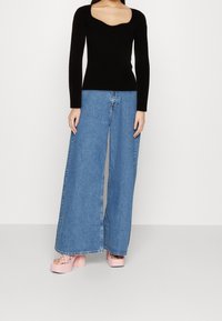 Schwarzes, geripptes Langarmoberteil mit quadratischem Ausschnitt, kombiniert mit hellblauen weiten Jeans und pinken, klobigen Plateausandalen.
