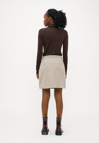 Pruun turtleneck-sviiter, heledast hallist seelik ja mustad pahklauknud, millel on punased aktsendid. Siledad tekstuurid, kohandatud lõige, minimalistlik disain.