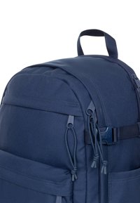 Mochila de tela azul marino con textura suave, cremalleras laterales, cuerdas ajustables y un asa en la parte superior. Cuenta con múltiples bolsillos.
