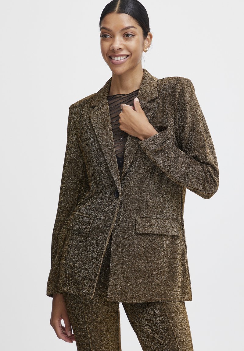 Metallisch goldener Blazer mit strukturierter Oberfläche, überzogen mit einreihiger Knopfleiste, zwei vorderen Taschen und einem einzigen Knopfverschluss.