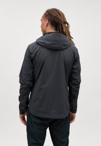 Sort vandtæt jakke med hætte, der har lange ærmer og elastiske manchetter. Glat tekstur med en let reflekterende finish.
