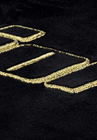 Čierny zamatový textil so zlatými vyšívanými líniami vytvárajúcimi písmená alebo tvary, predvádzajúci jemnú textúru a kontrastné farby.