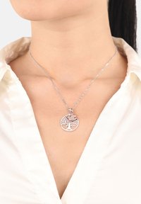 Söljtree av liv-hängehalsband med intrikat utskärningsdesign, med en roséguldaccent, preciserat på en ljus skjorta.