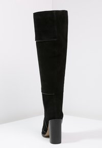 Svart mocka knähög stövel med en strukturerad form, utrustad med en hög klack och rena stygn längs sömmen.