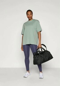 Heledad rohelise t-särgiga, tumelilla retuusid ja valged tossud. Must duffel-kott kahe käepidemega. Lihtne ja mugav spordiriietus.