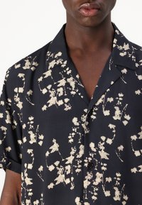 Short-sleeve shirt in dark blue fabric with a floral print in cream. Features a camp collar and a buttoned placket. Soft texture.