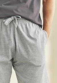 Grå sweatpants med elastisk midjeband och dragsnodd, med sidofickor och ett mjukt, texturerat tyg. Matcher med en mörk skjorta.