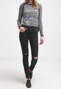 Vaqueros pitillo negros con las rodillas rasgadas combinados con un suéter gris de manga larga con un patrón texturizado de rayas y acentos negros.