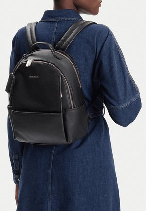 Zaino in pelle nera con design arrotondato, doppia cerniera e tasca frontale. Texture liscia con tracolle regolabili.