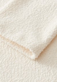 Asciugamano bianco in spugna piegato che mostra una morbida superficie a anelli e un sottile motivo geometrico sul tessuto.