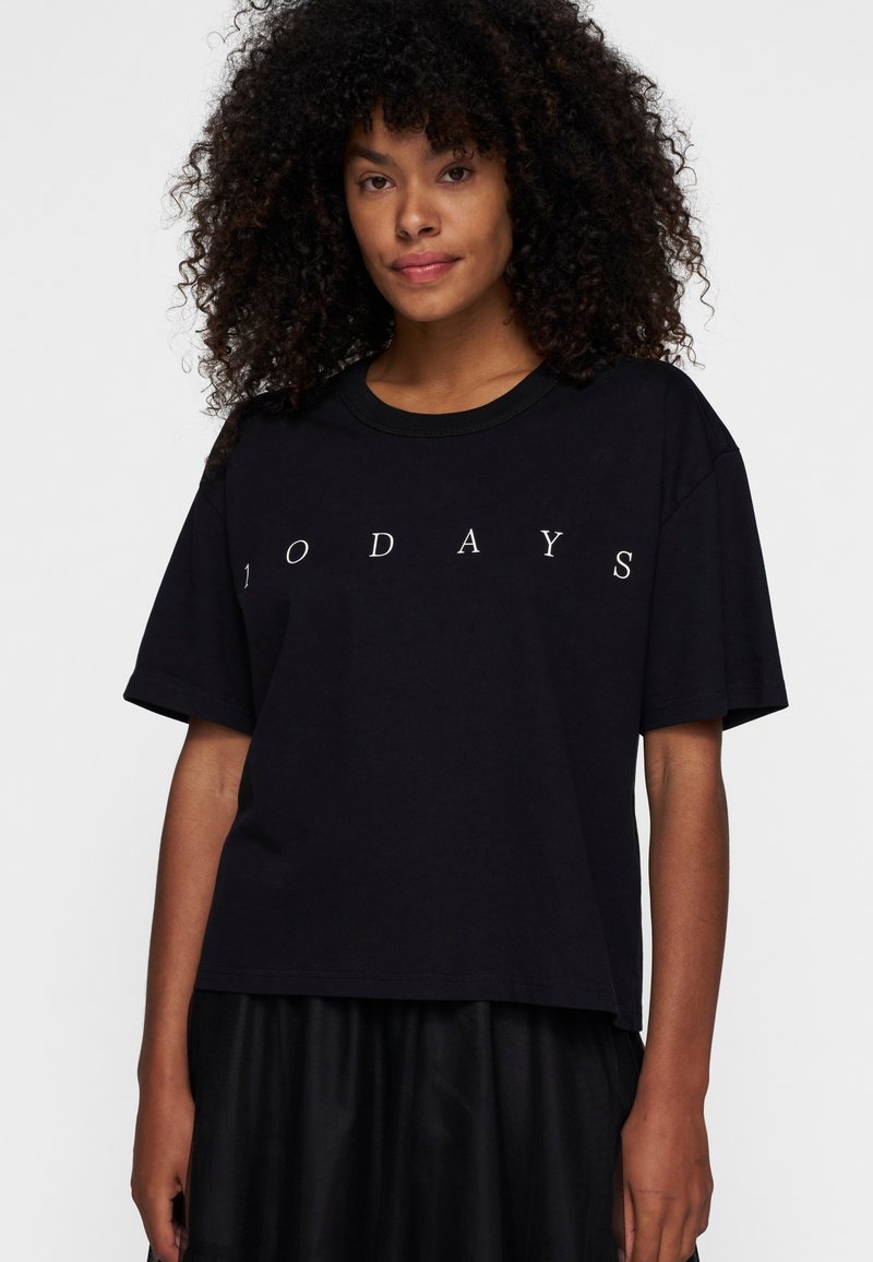 Camiseta negra de gran tamaño hecha de algodón, con mangas cortas y cuello redondo, que presenta la palabra "TODAYS" en texto blanco en la parte delantera.