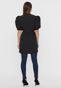 Schwarzes Kleid mit puffierten kurzen Ärmeln, tailliertem Gürtel und gerader Silhouette. Trägt man über dunkeldorf Blauen Skinny Jeans und schwarzen High Heels.