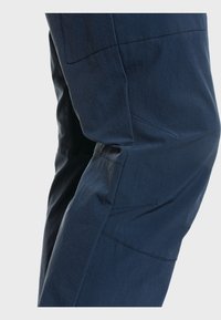 Marineblaue Hose aus leichtem Stoff mit glatter Textur, schrägen Nähten und praktischen Seitentaschen.