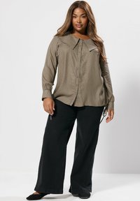 Camicia button-up a quadri marrone e crema con colletto ampio, abbinata a pantaloni neri a gamba larga. Tessuto morbido con vestibilità rilassata.