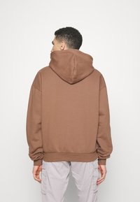 Felpa con cappuccio marrone dalla vestibilità rilassata, con spalle scese e polsini a coste. Tessuto morbido con un design minimalista.