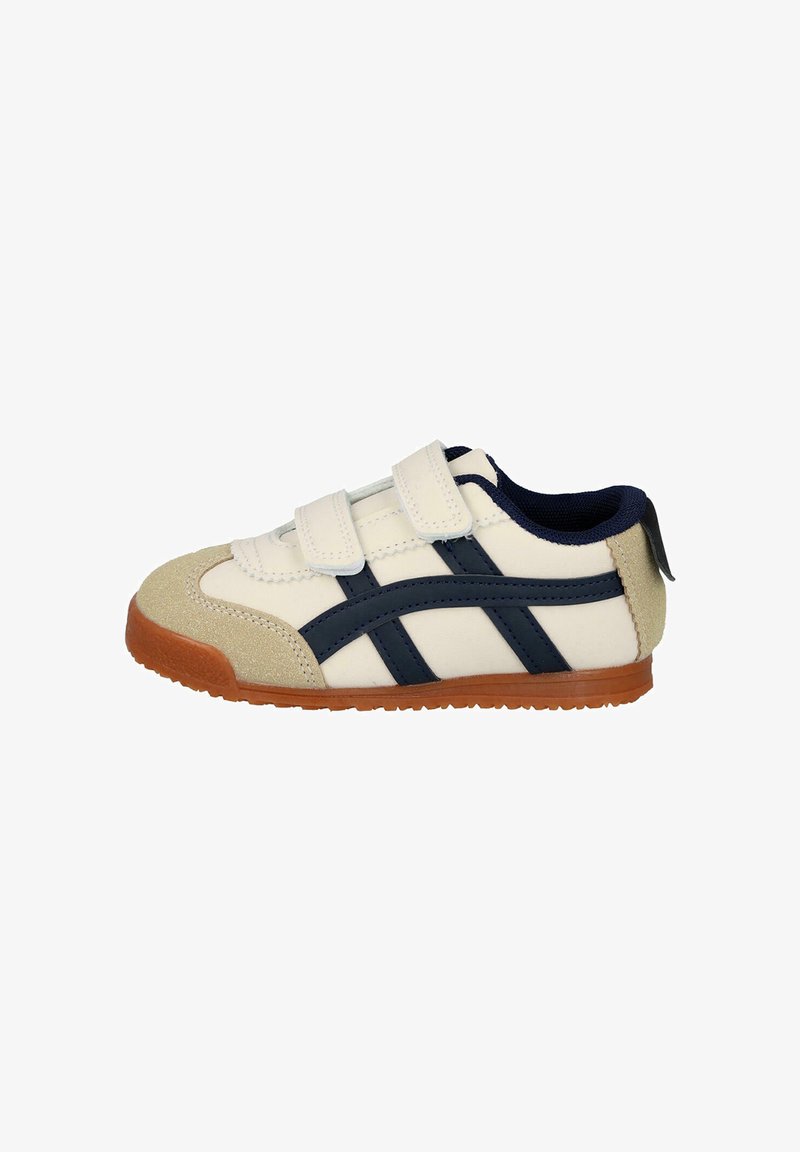 Zapatilla blanca con rayas en azul marino, correas de velcro y puntera de gamuza color beige. Suela de goma en marrón, con detalles texturizados.