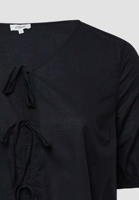 Schwarze Bluse mit V-Ausschnitt, die ein Kordelzugdetail an der Vorderseite und kurze Puffärmel aufweist. Hergestellt aus leichtem, strukturiertem Stoff.